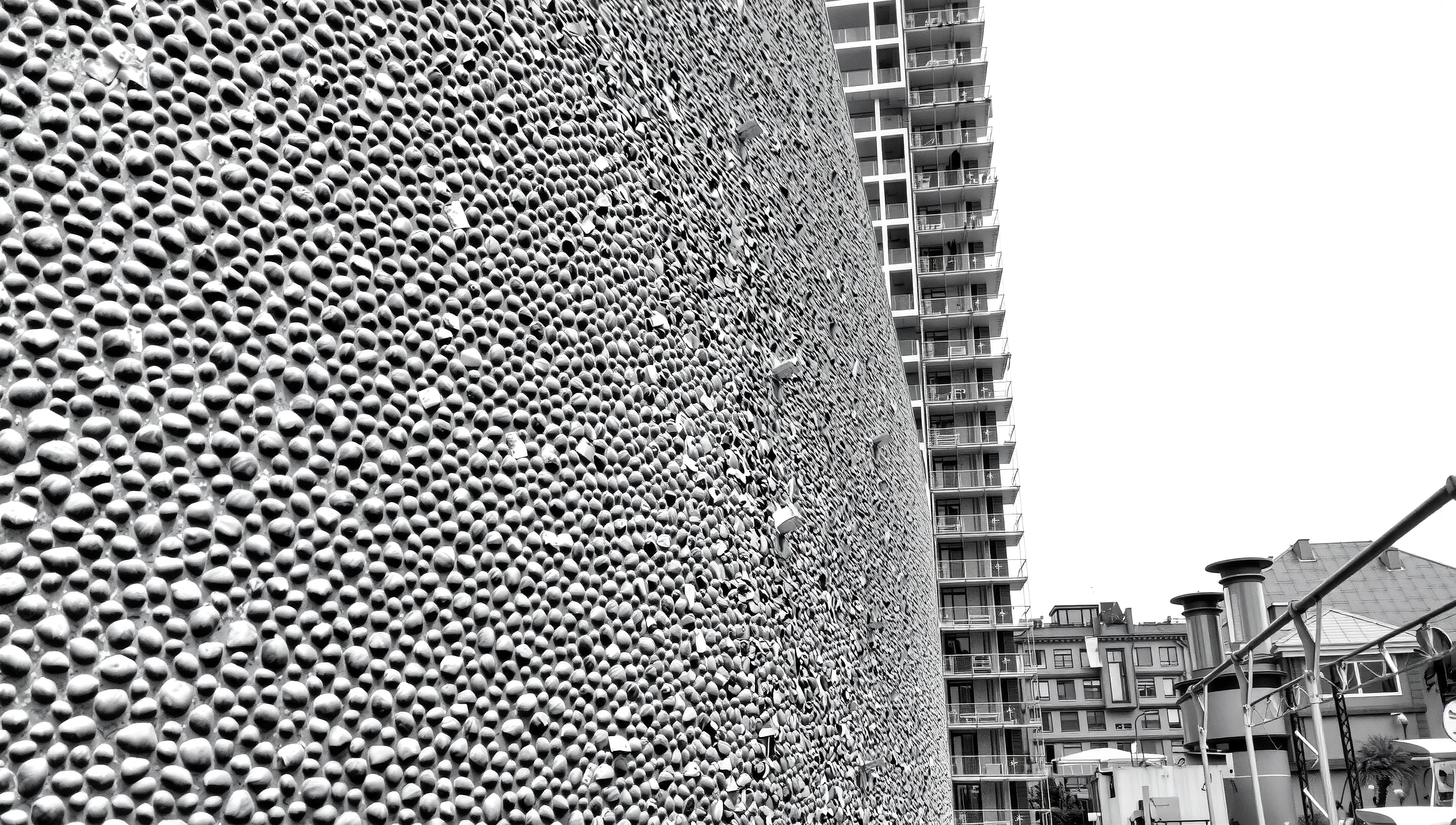 A textured stone wall juxtaposed with a modern apartment building, highlighting architectural contrasts in an urban environment.