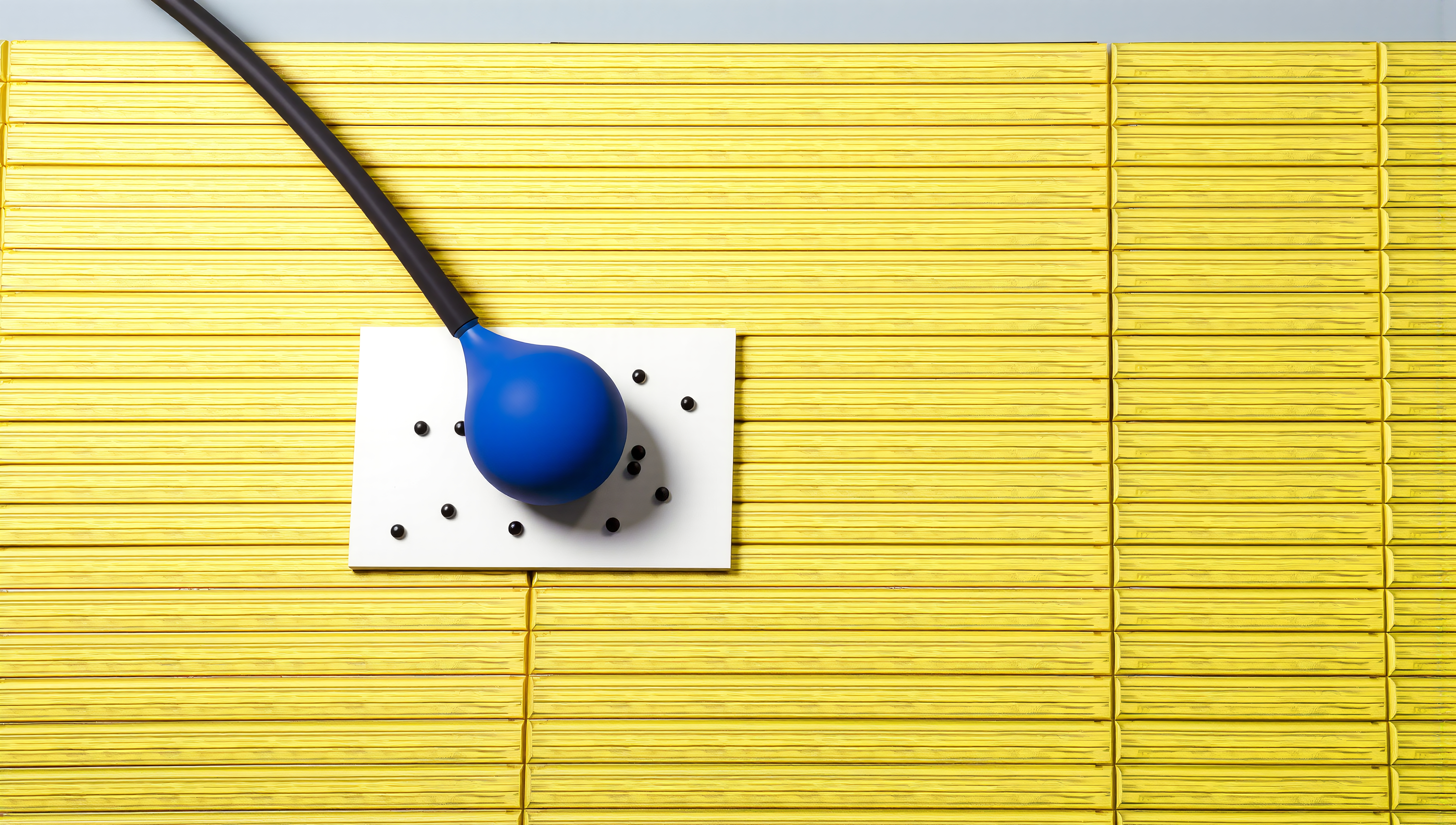 A blue rubber bulb with a black tube on a white plane, scattered with black spheres, atop yellow blocks.