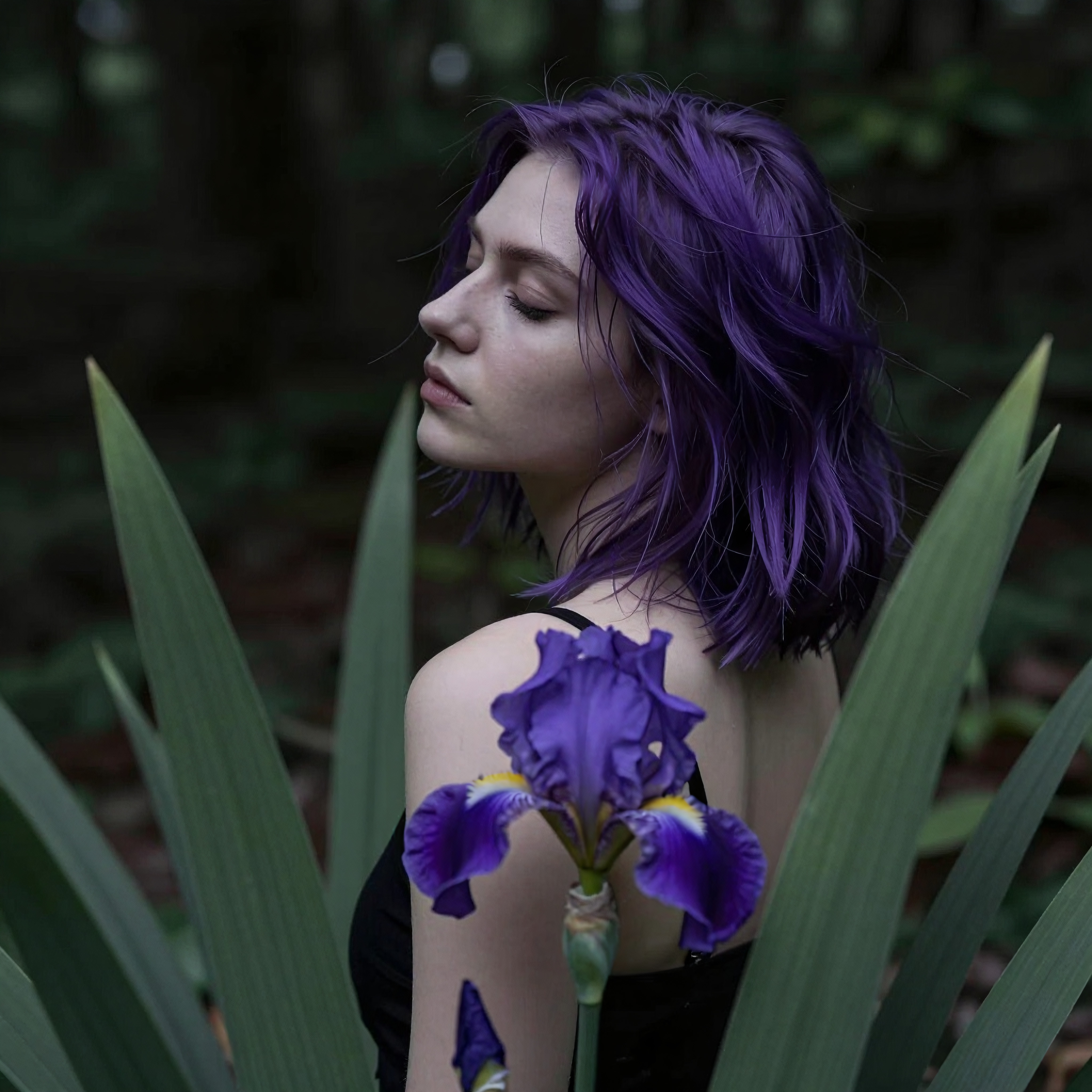 A woman with purple hair surrounded by lush greenery and a striking purple iris.