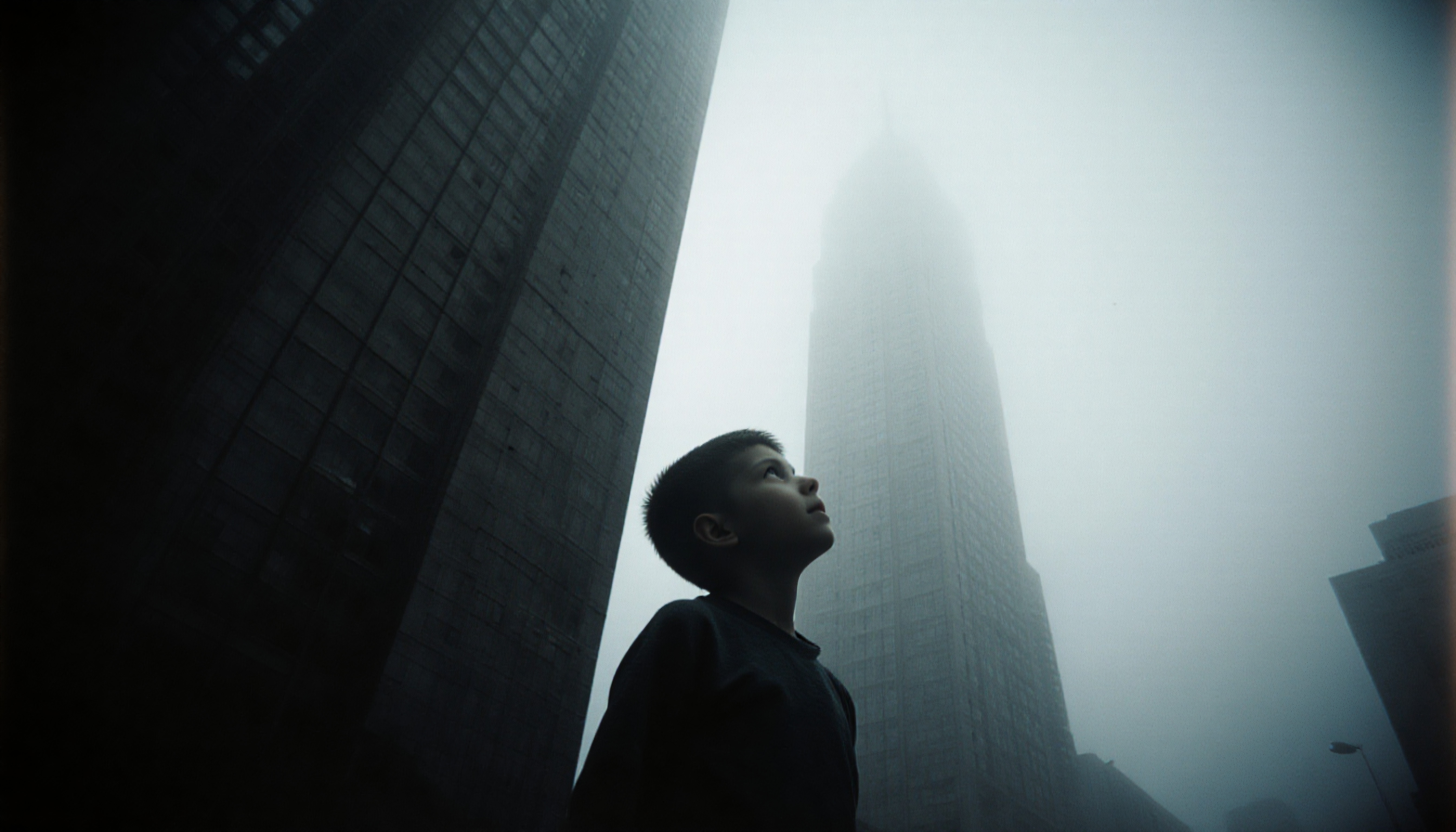 A young boy gazes upward amidst towering skyscrapers enveloped in fog, evoking a sense of wonder and urban exploration.