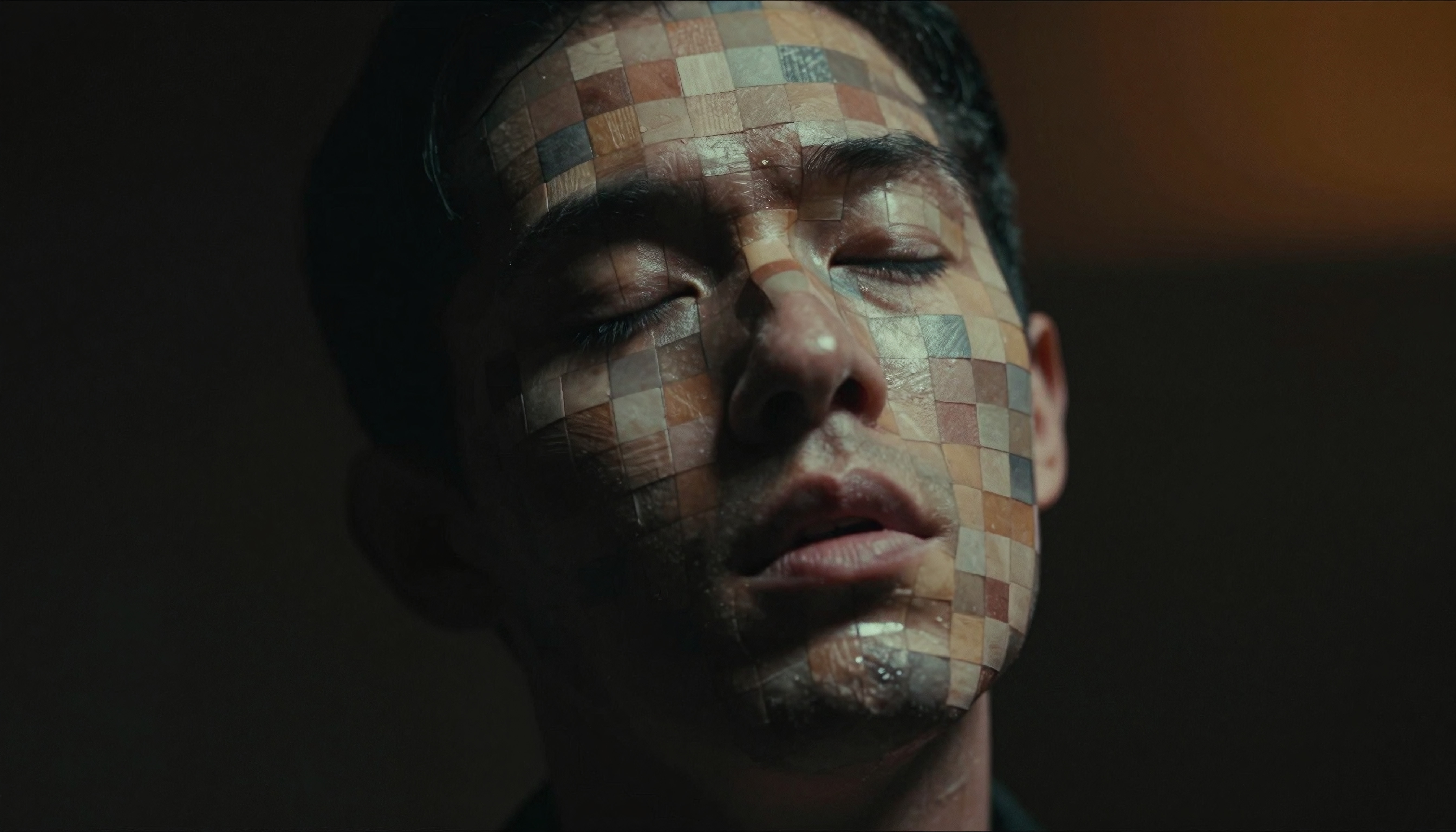 Close-up of a man with multicolored mosaic squares on his face creating an artistic and introspective visual effect.