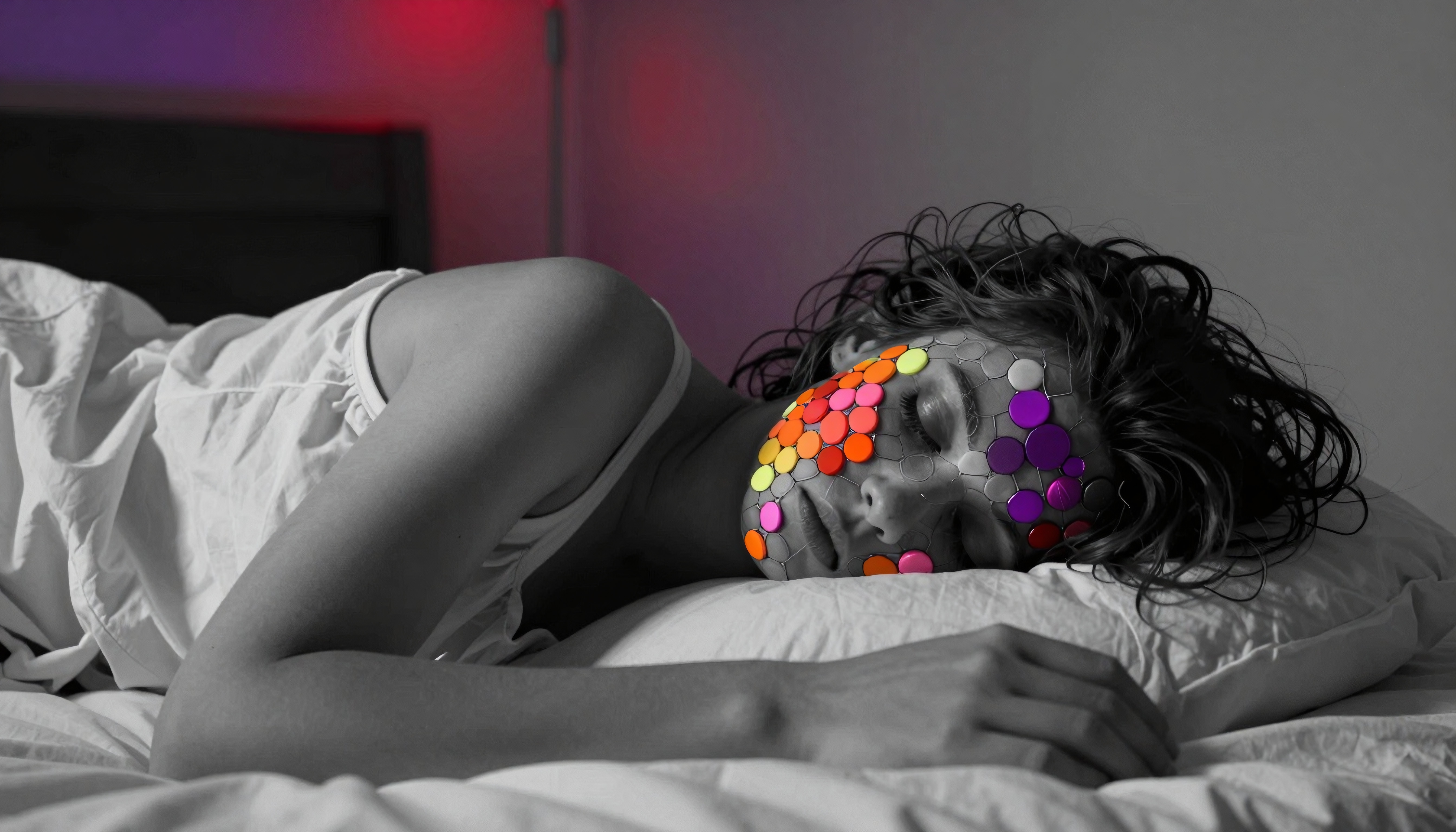 A person peacefully asleep with a colorful, artistic mosaic on their face, set against a grayscale bedroom background with subtle red lighting.