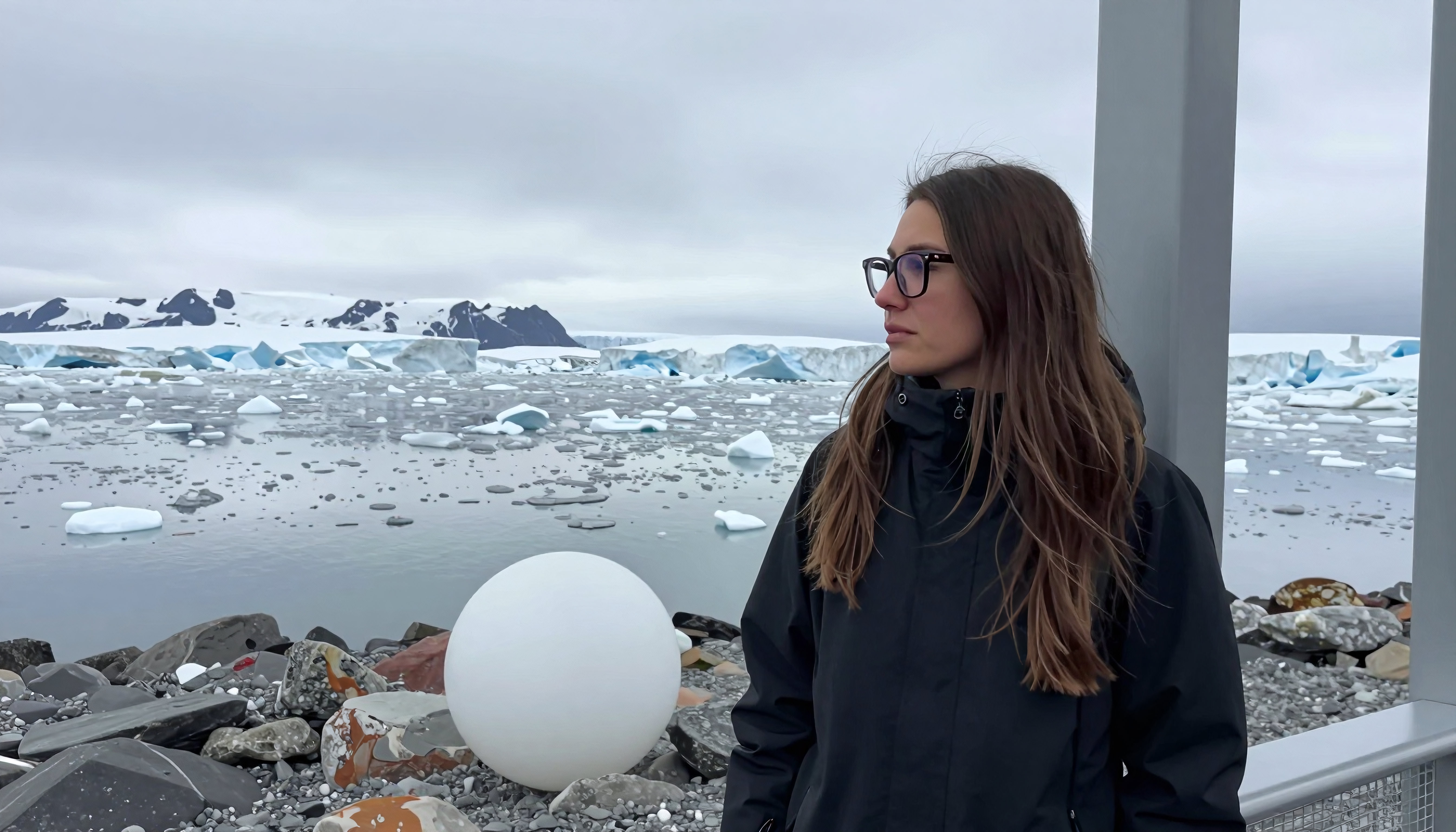 Woman in black coat observing icebergs in a cold, overcast Arctic landscape.