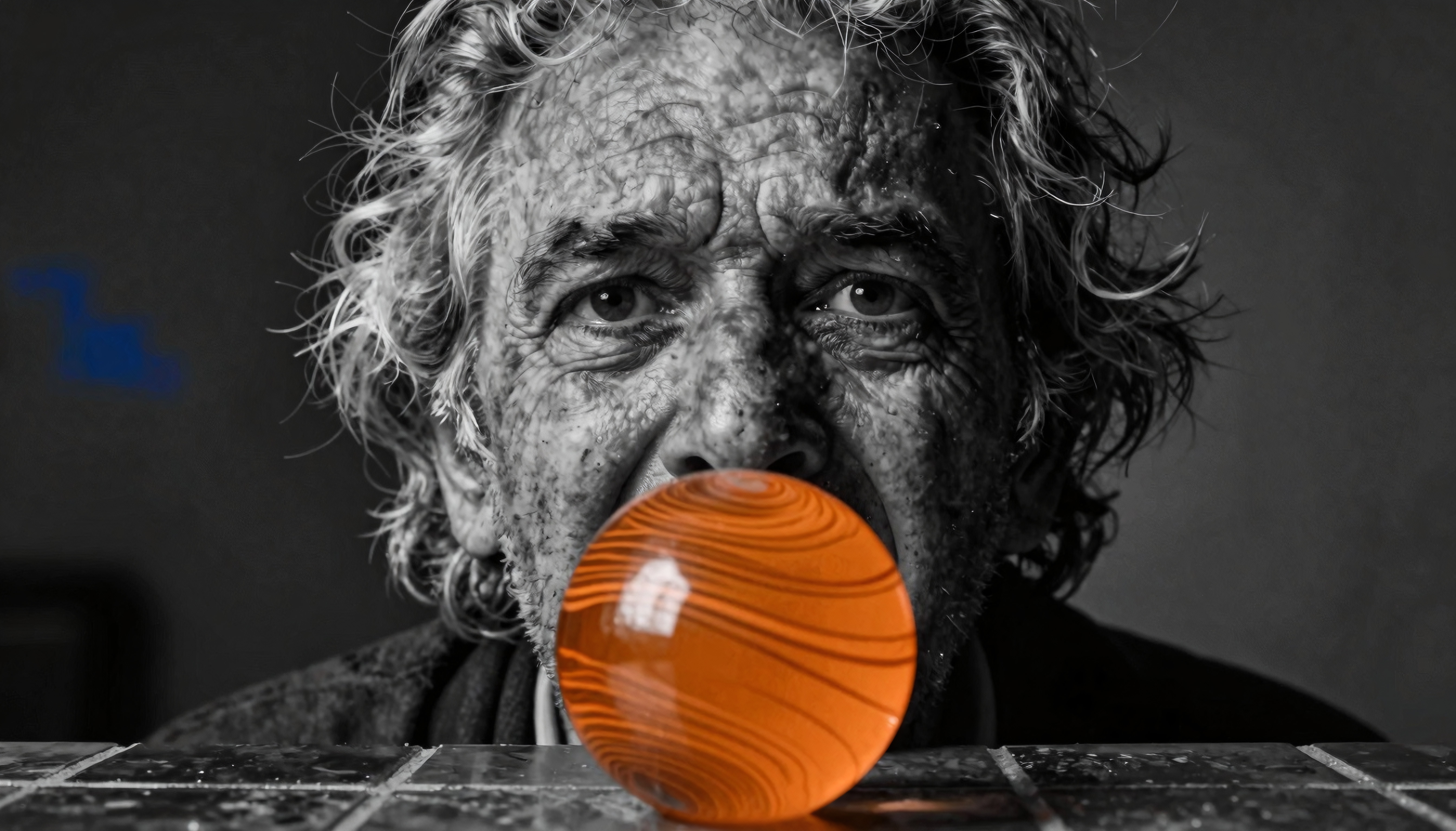 Elderly man observing an orange sphere in monochrome setting.