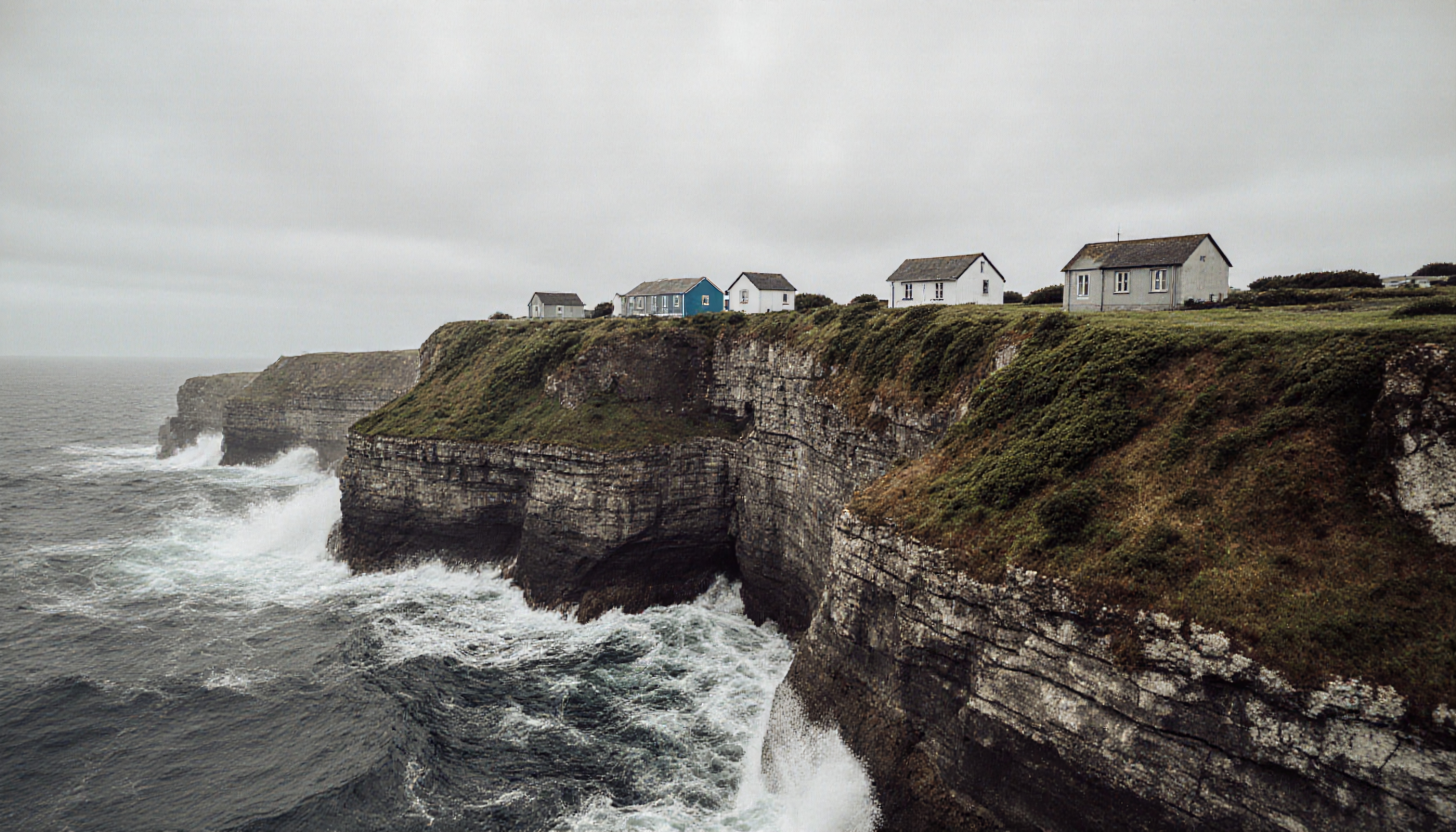 Coastal cliffside with houses and crashing waves.