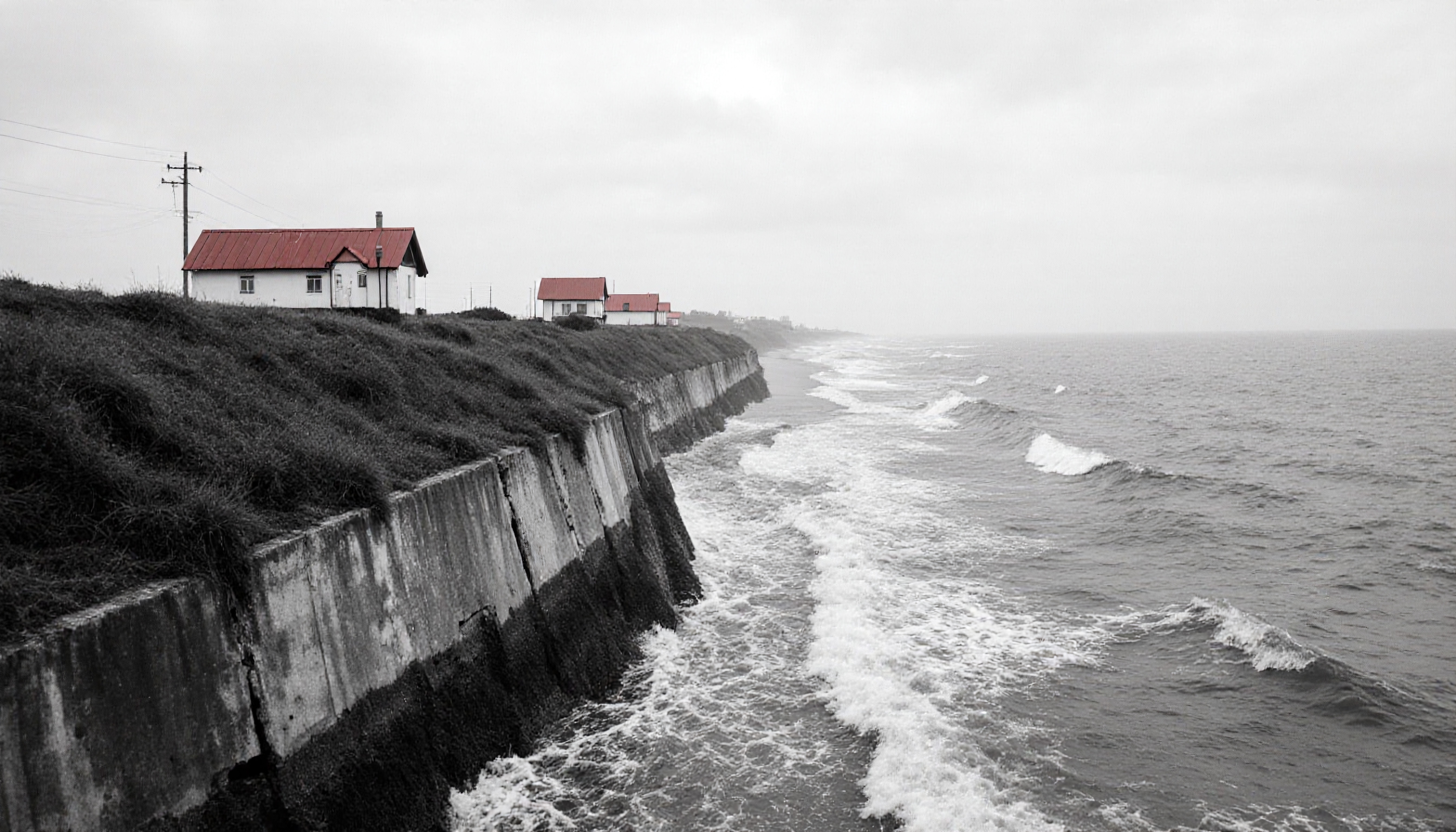 A peaceful coastal scene with houses featuring prominent red roofs, set against a monochrome backdrop of stormy seas and an overcast sky.