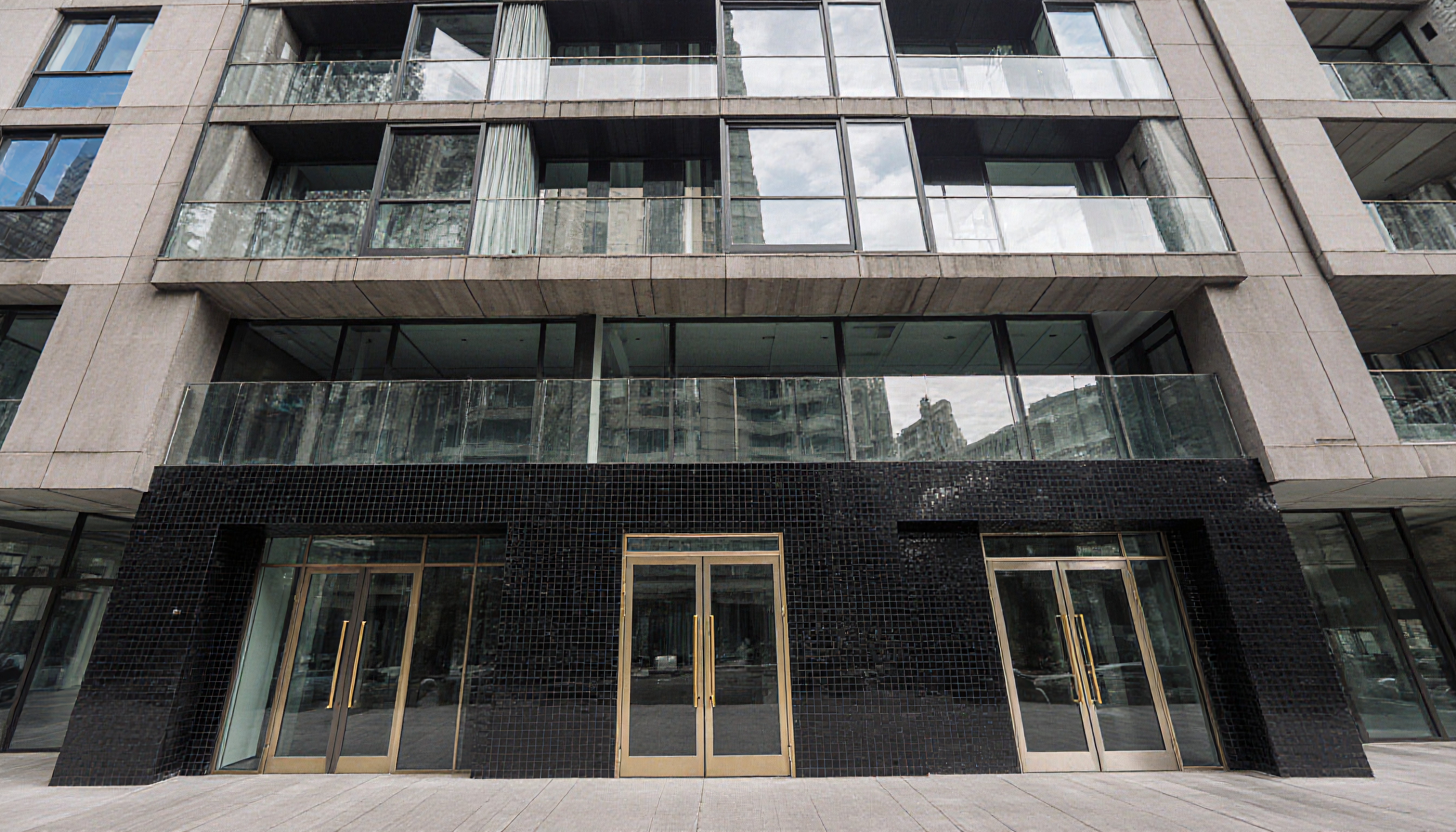 Modern urban building entrance with glass balconies and reflective facade highlighting contemporary design.