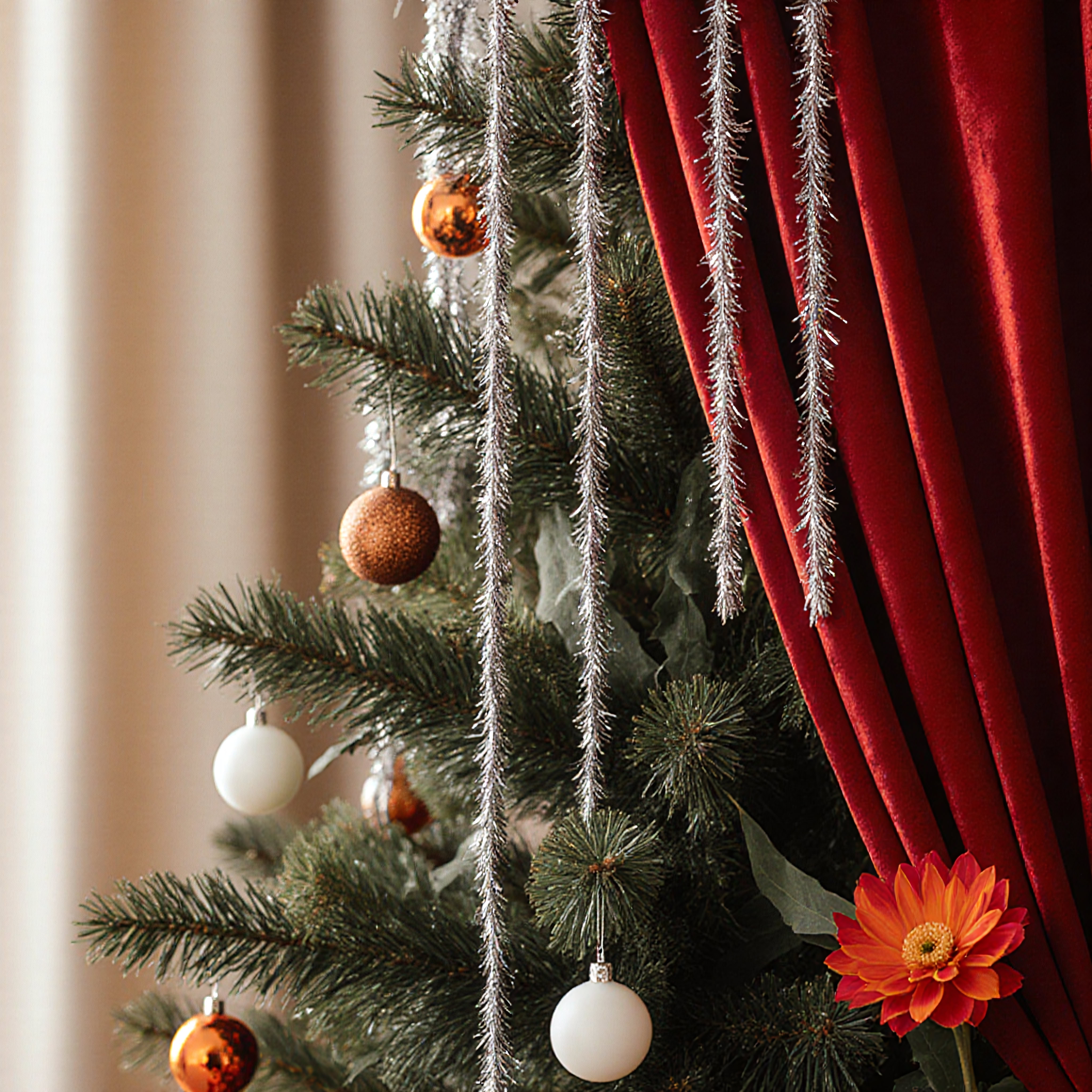 Christmas tree adorned with ornaments, tinsel, and orange-red flower next to red curtains.
