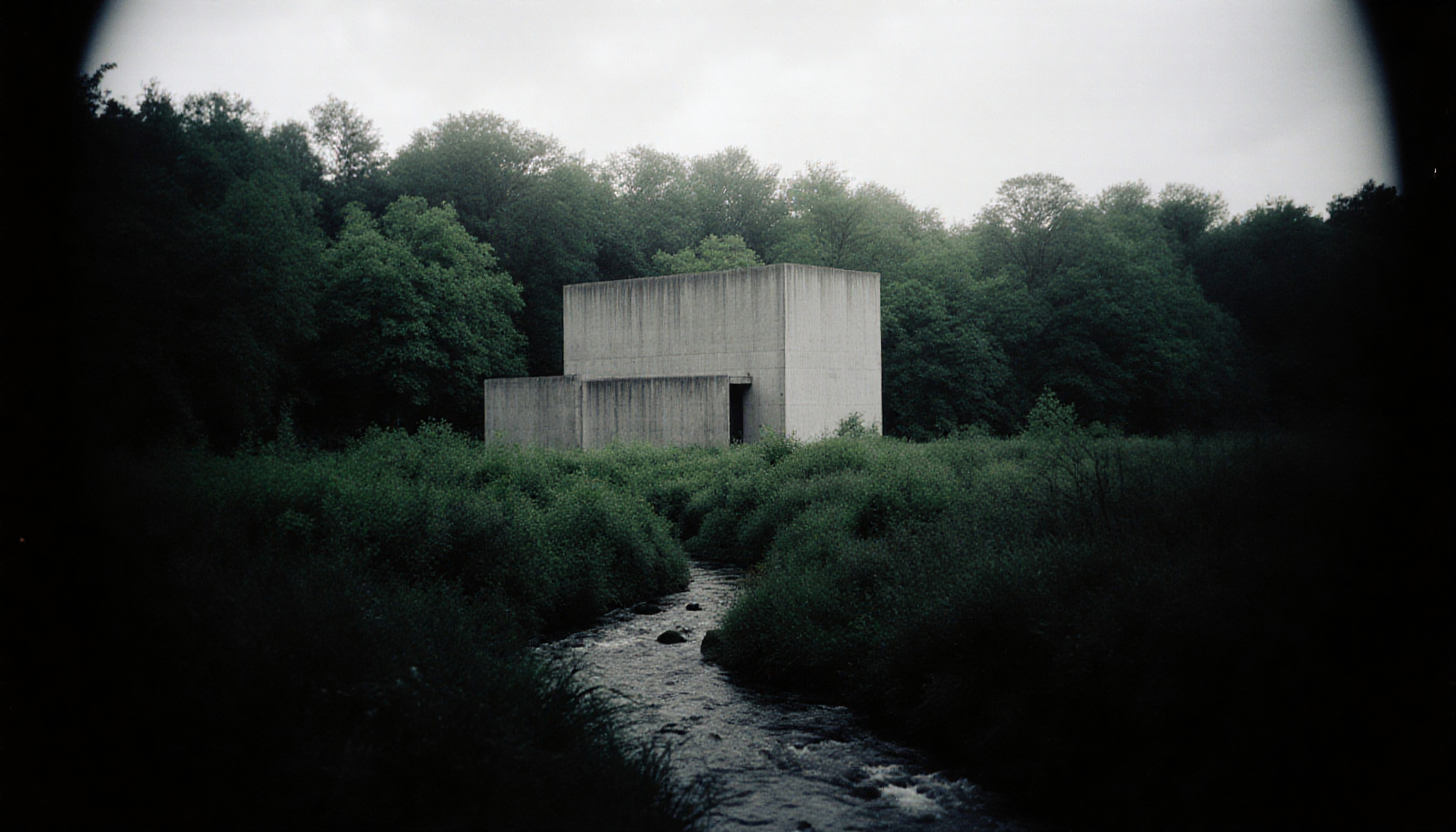 An isolated concrete building amidst lush forest with a flowing stream.