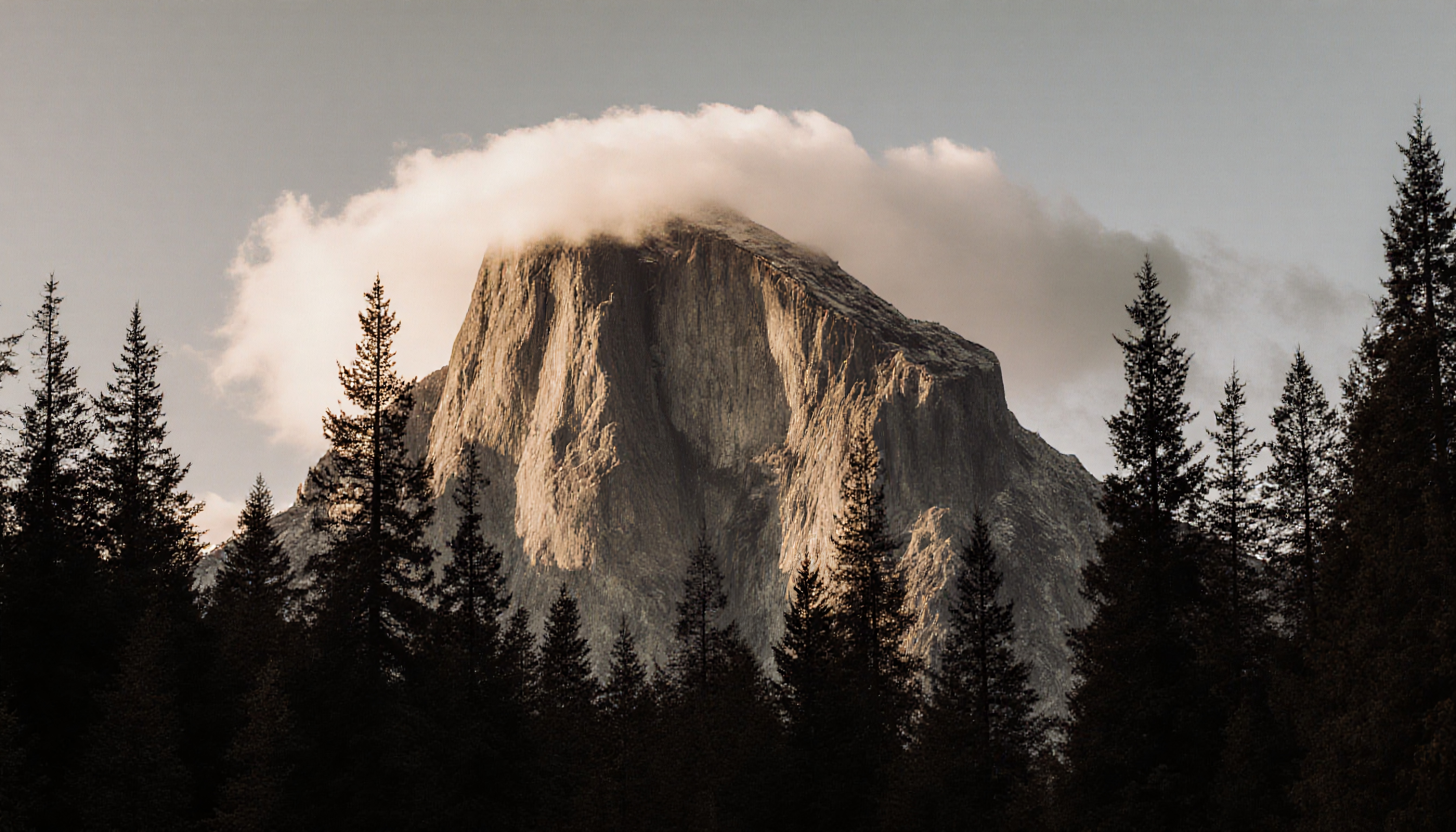 A majestic mountain peak enveloped by clouds with a forest below, set in a tranquil natural landscape.