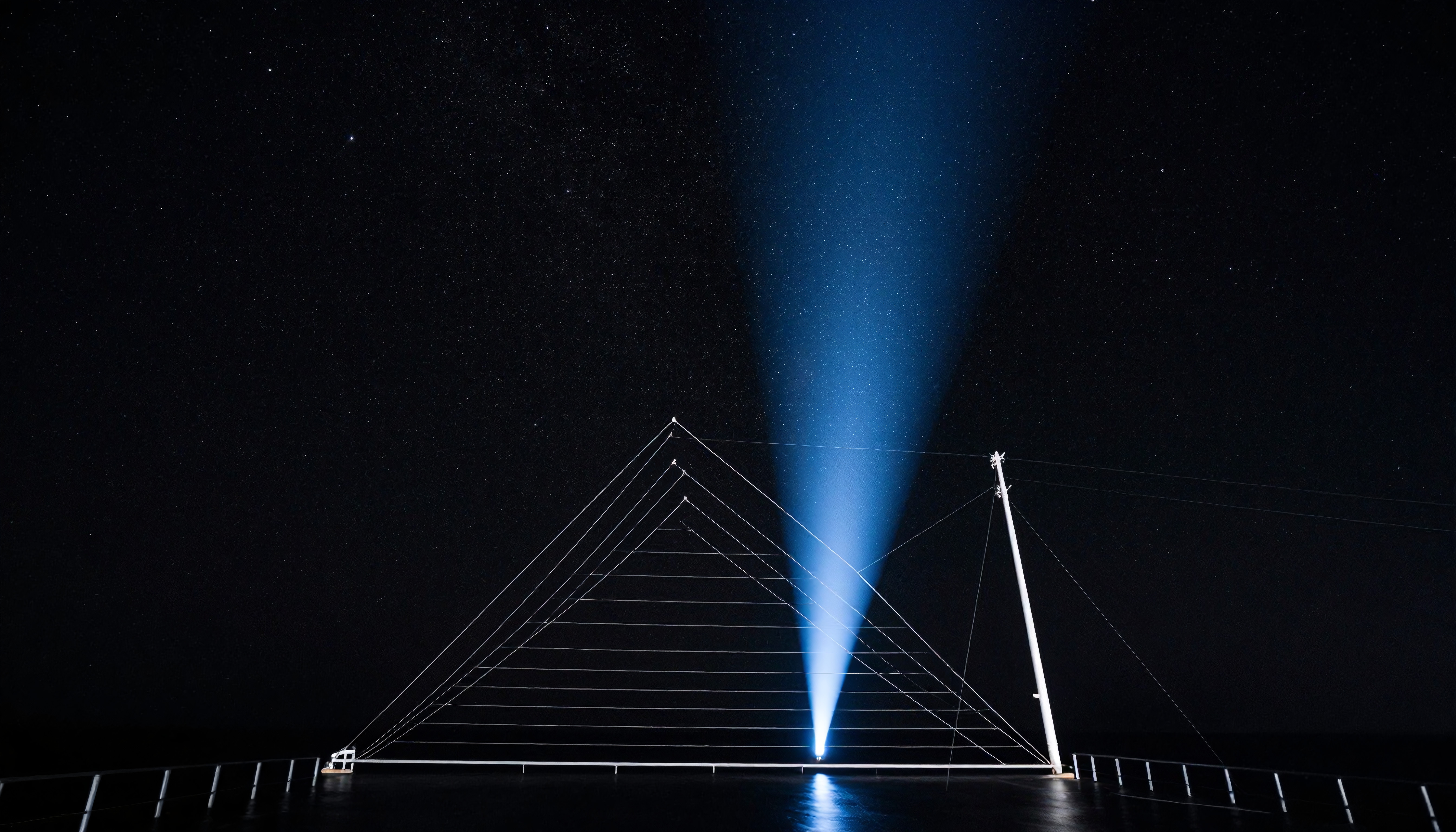 A wide searchlight beam illuminates a triangular structure against a starry night sky.