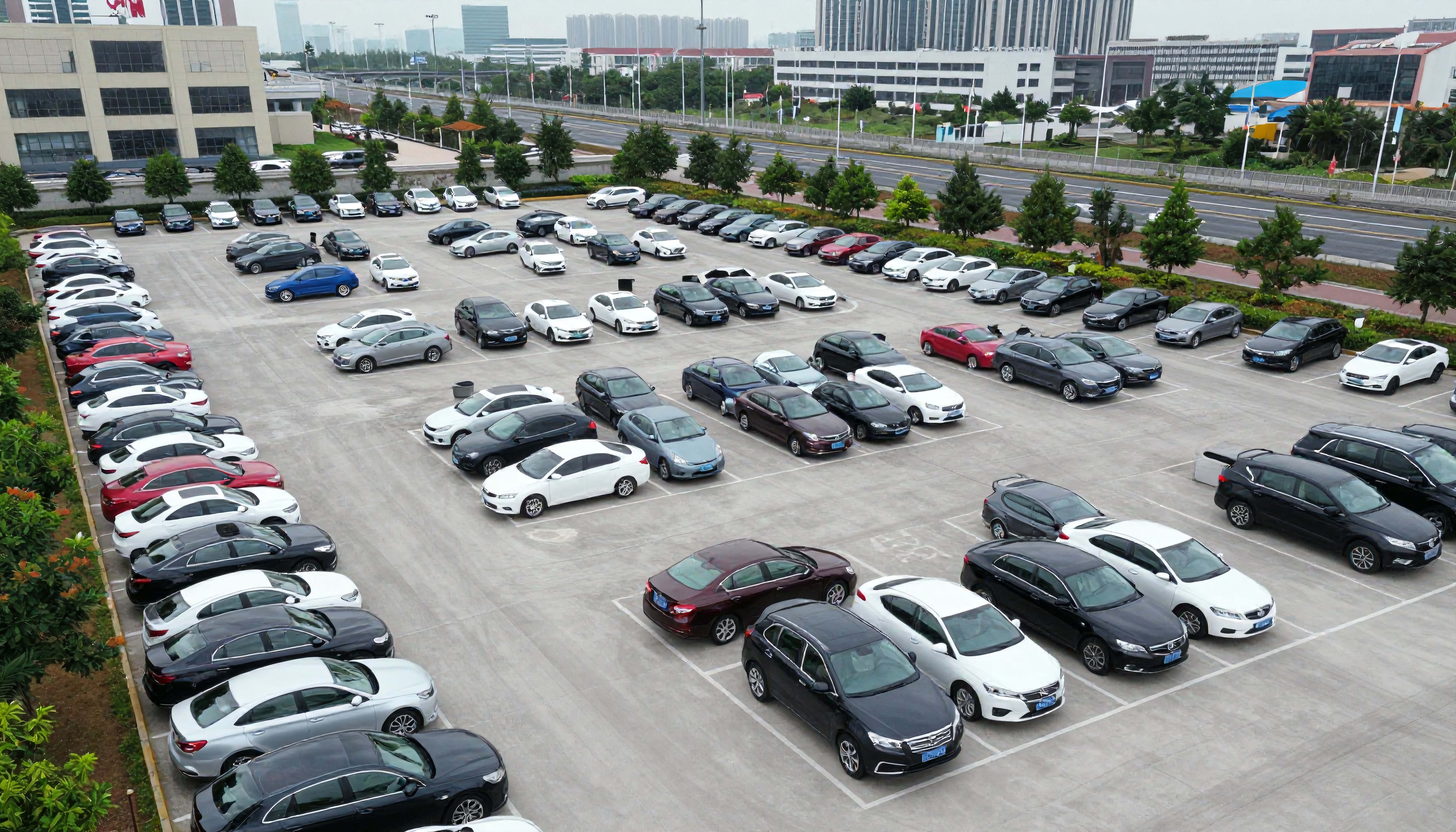 A well-organized urban parking lot filled with various cars and surrounded by tall buildings and greenery.