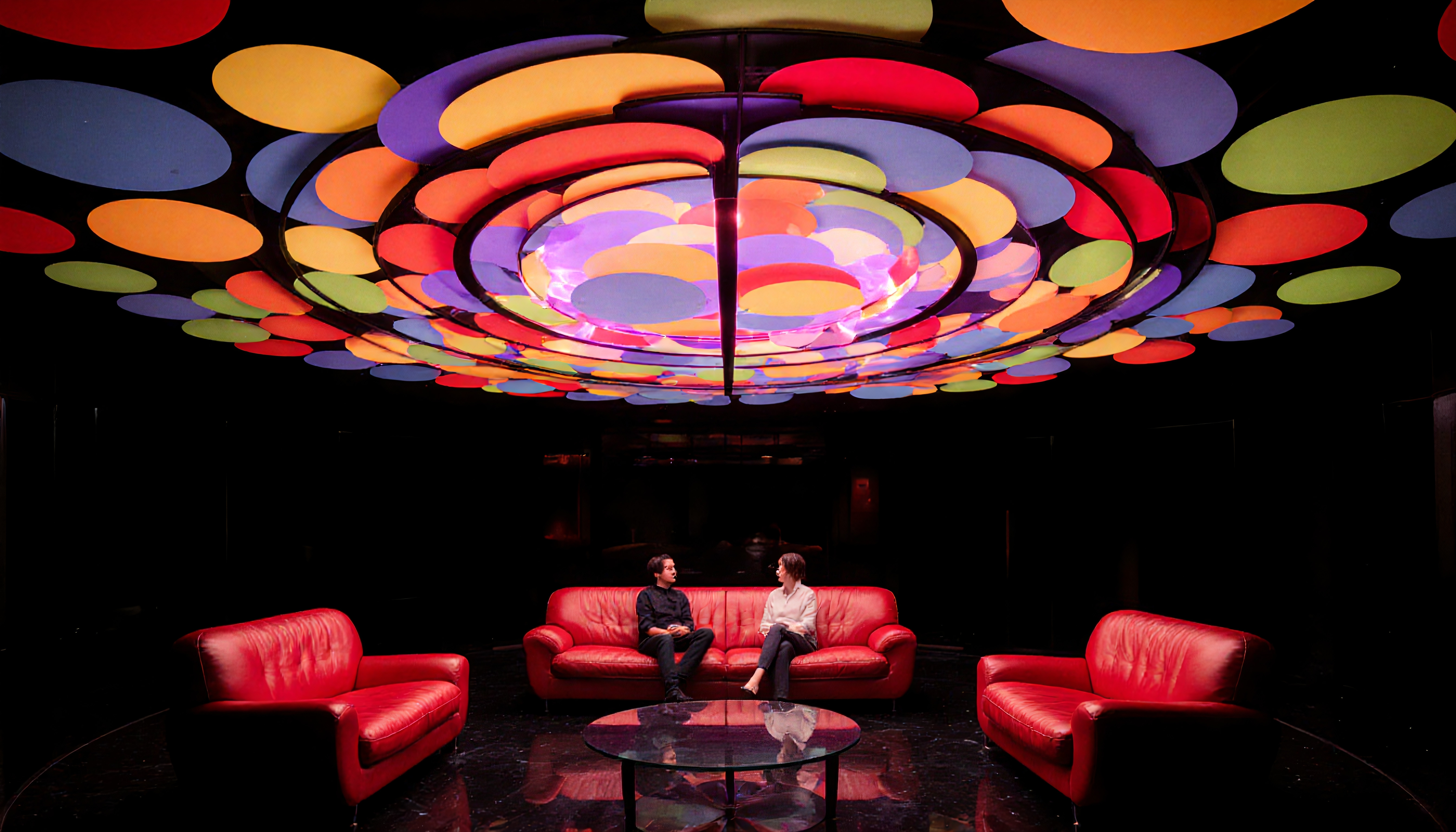 A vibrant modern lounge with colorful circular ceiling panels and red sofas.