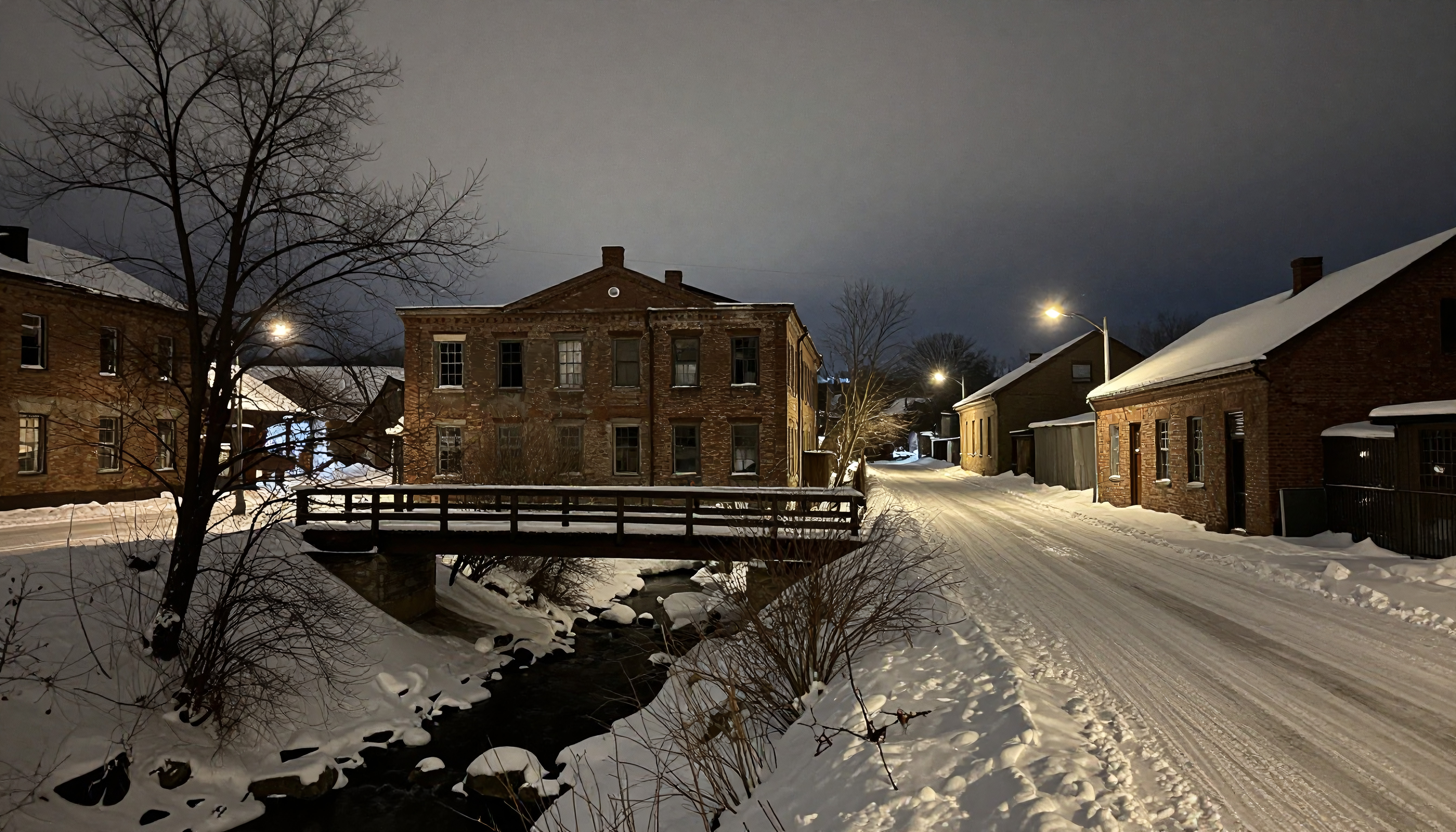 Snowy winter night bridge over creek in old brick town