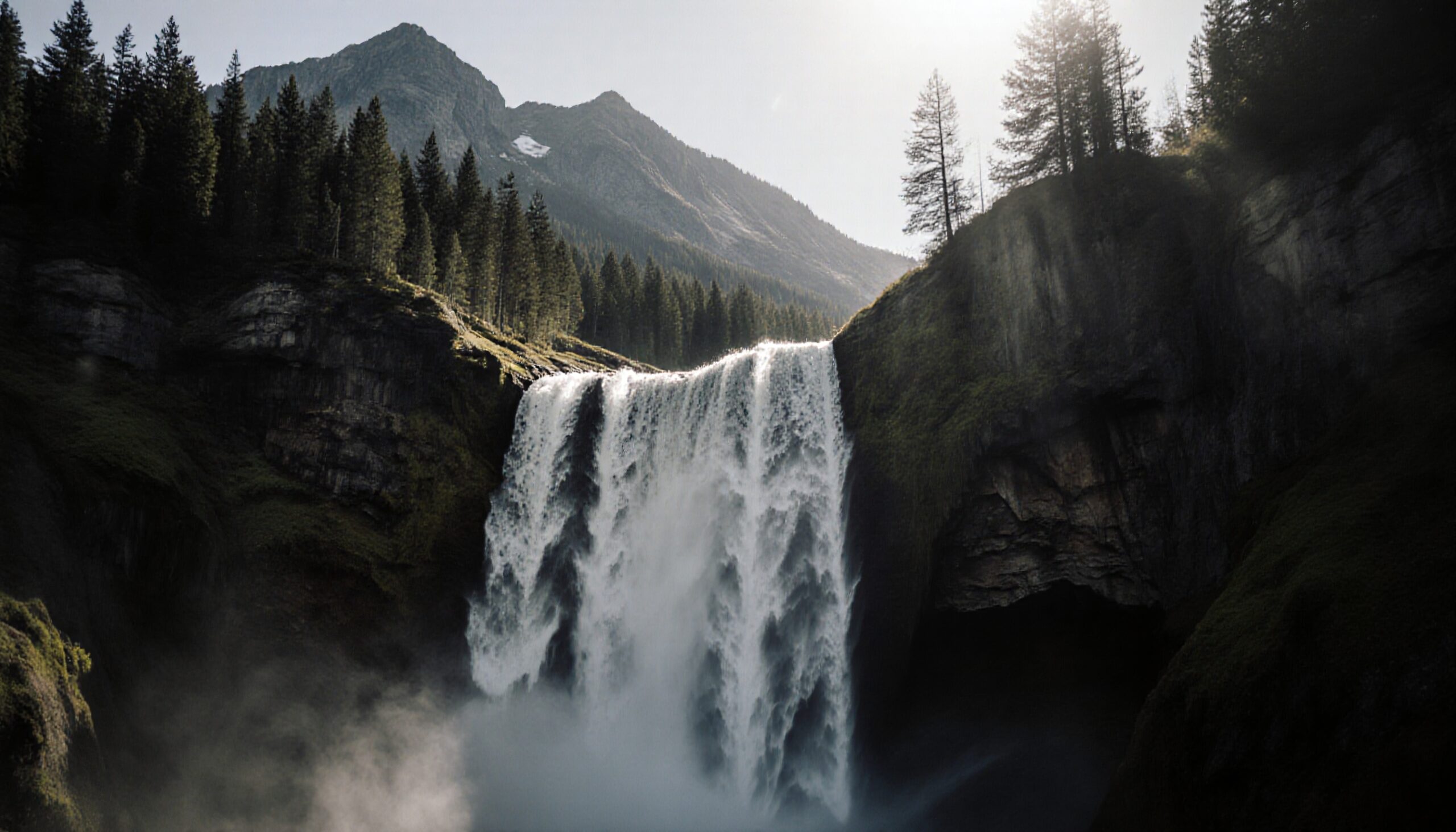 A majestic waterfall flowing down a cliff surrounded by forested mountains in sunlight.