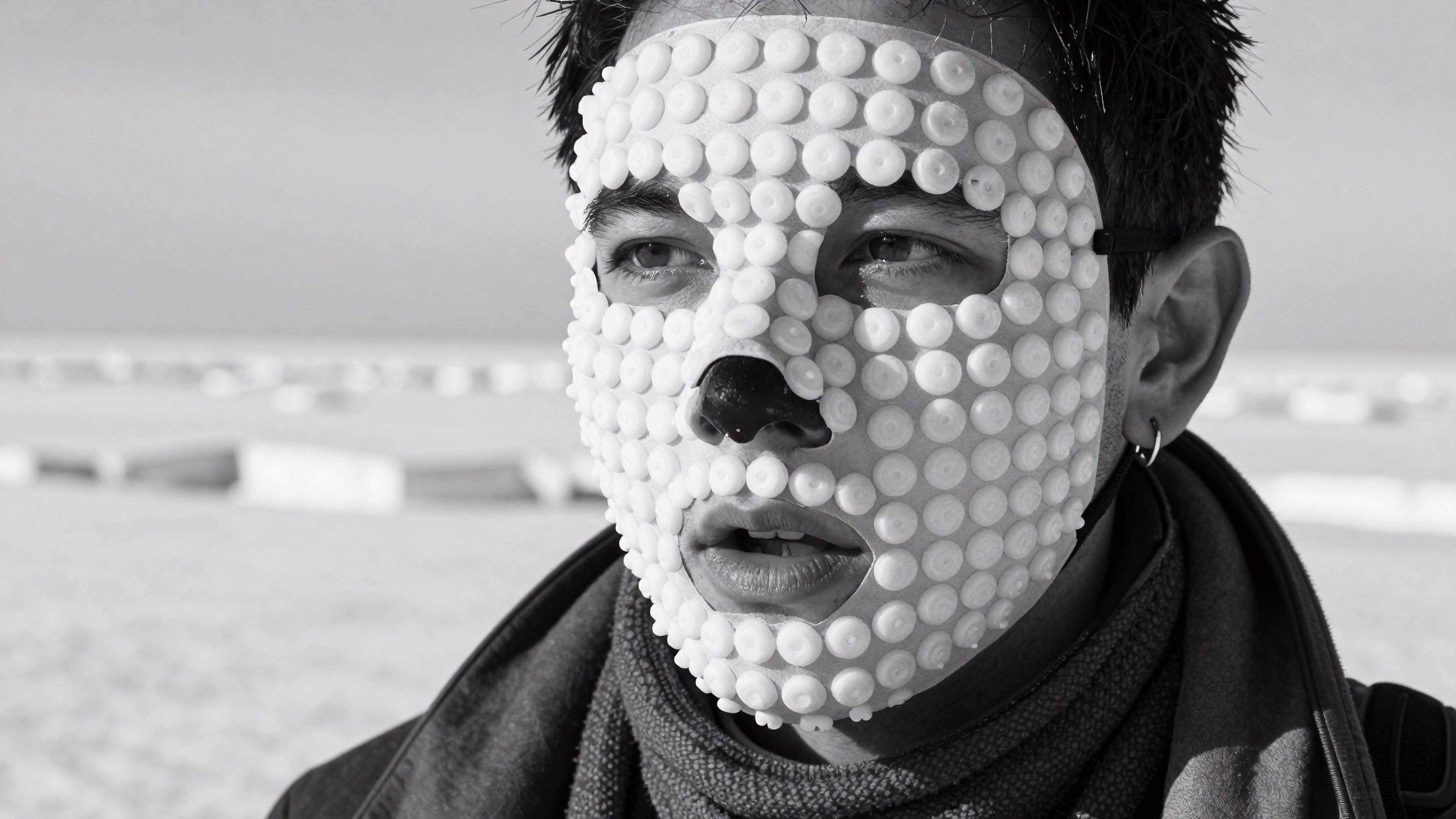 Man wears beaded mask on snowy background, artistic black and white portrait