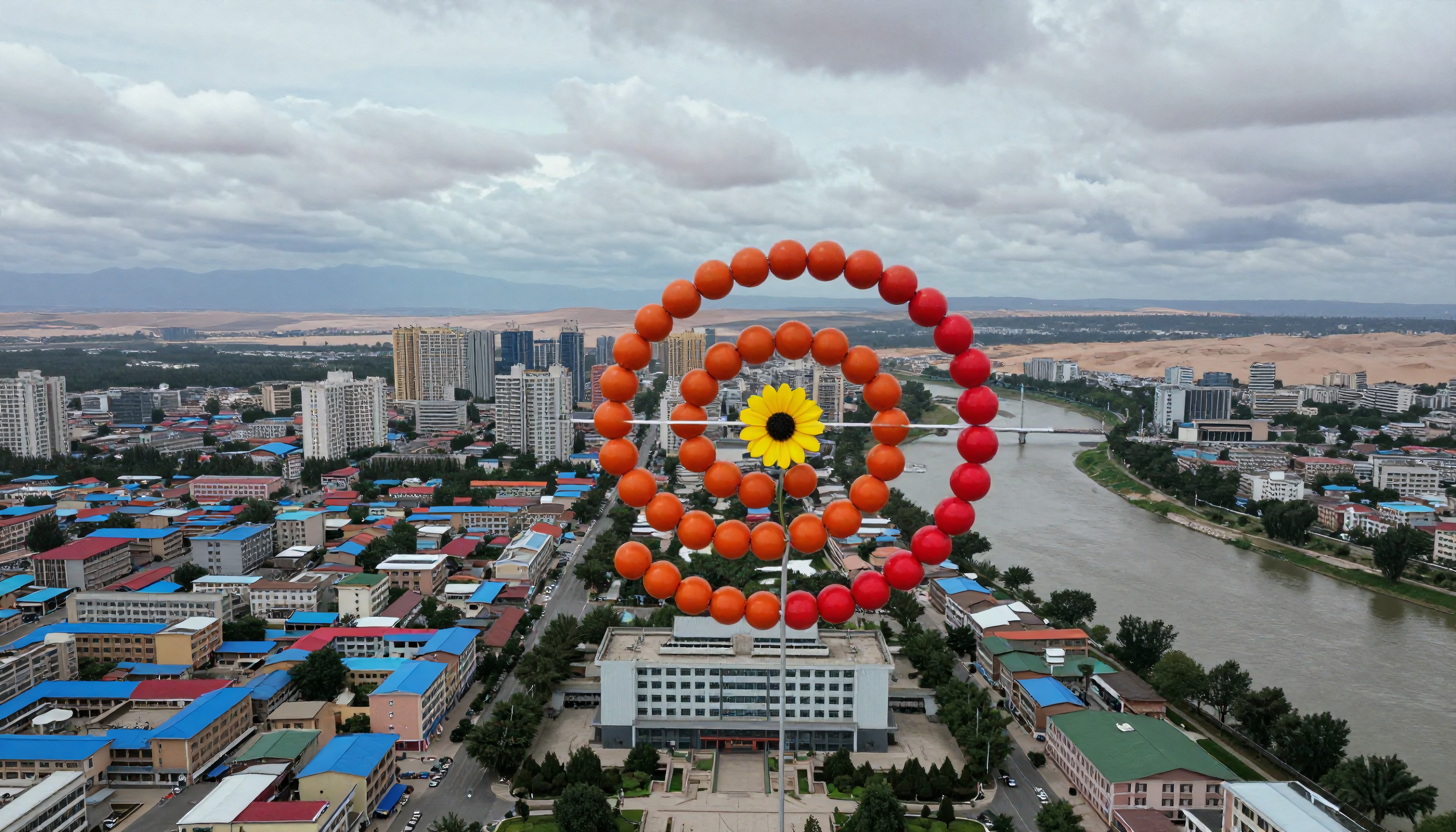 A large colorful spiral overlooks a vibrant cityscape with a river and buildings.