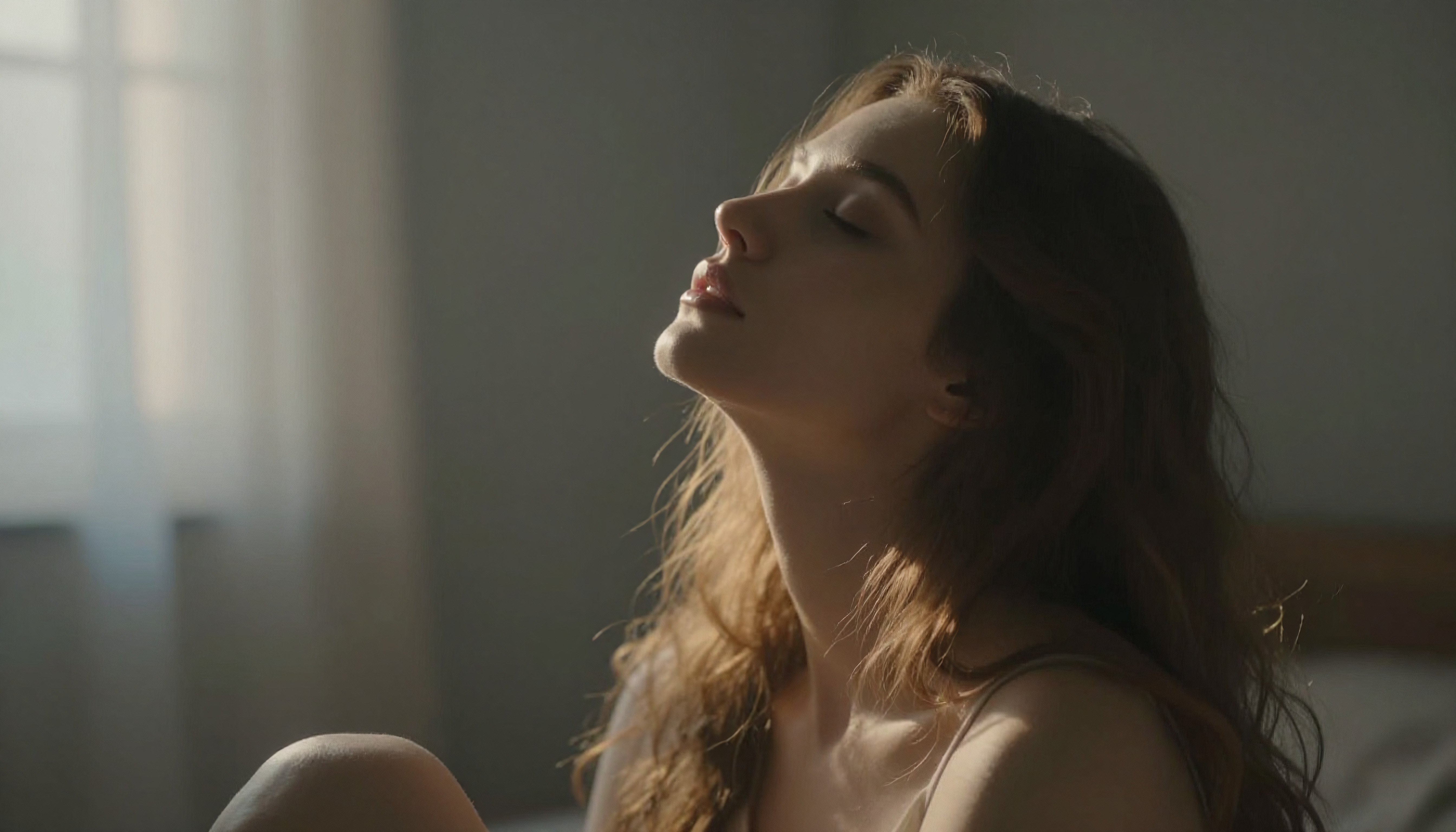 A woman with closed eyes basking in gentle sunlight, exuding calm and peacefulness in a softly lit room.