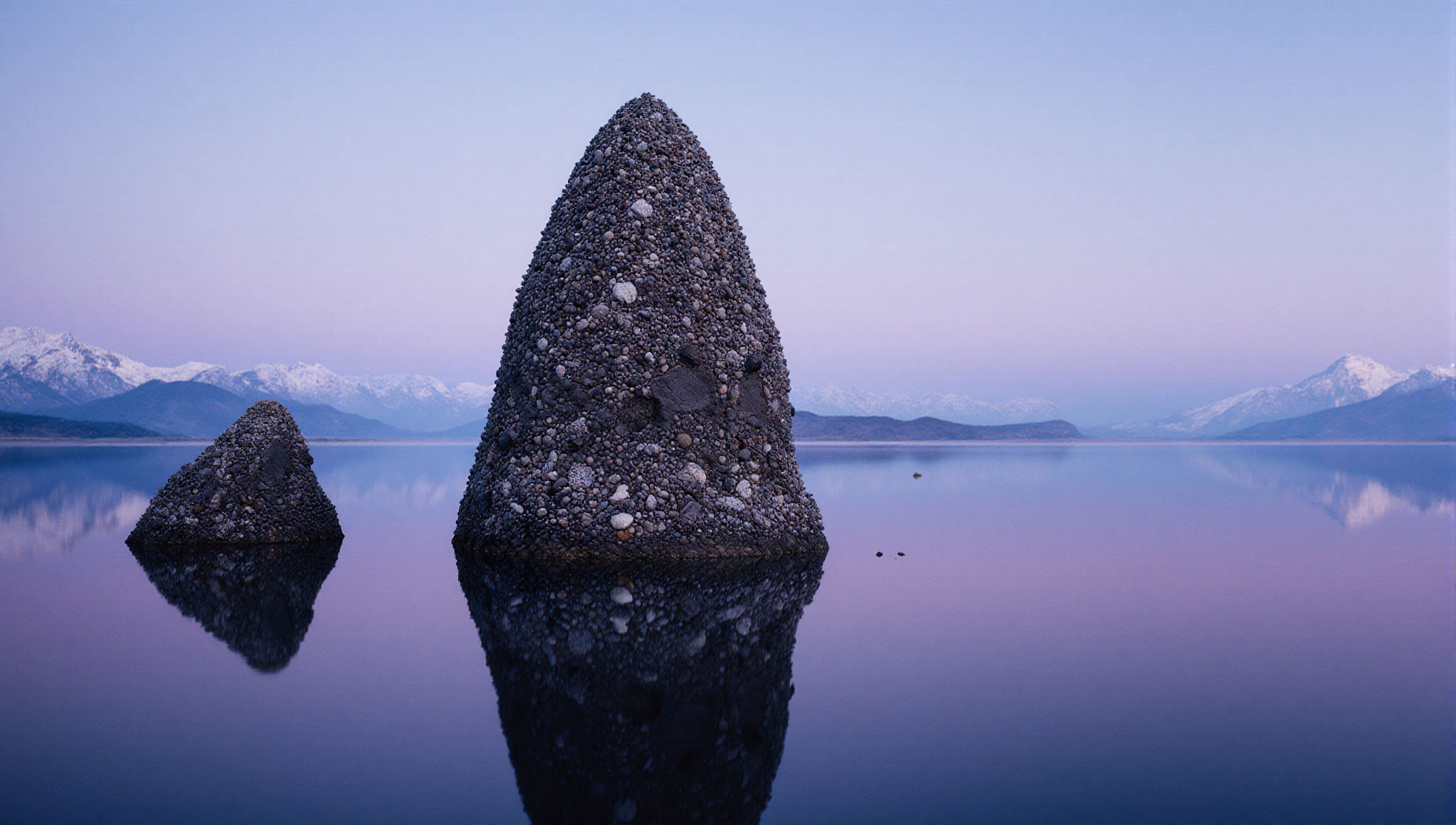 Reflective rock formation on serene lake with mountain view.