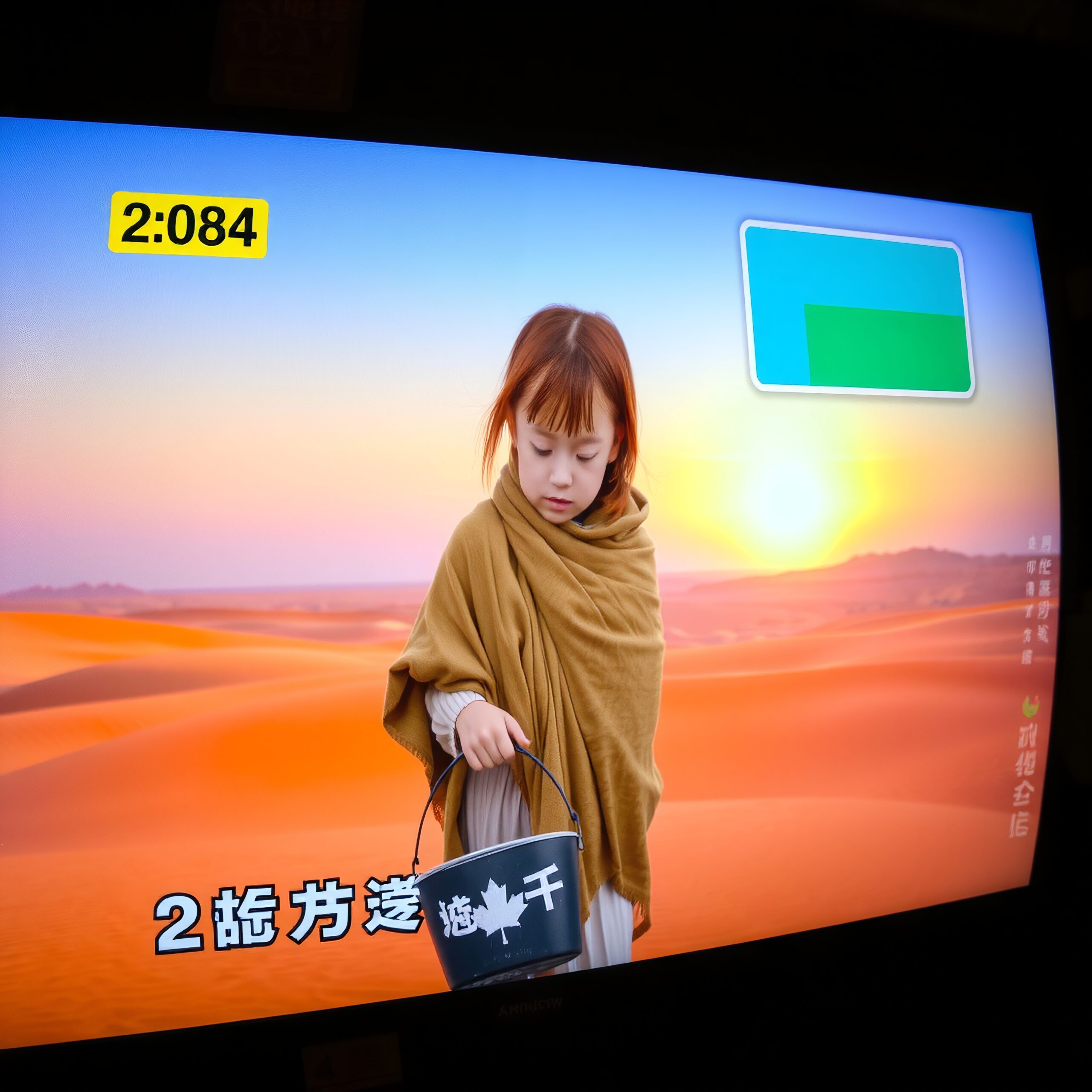A young girl in a shawl gazes at a bucket in a desert at sunset.