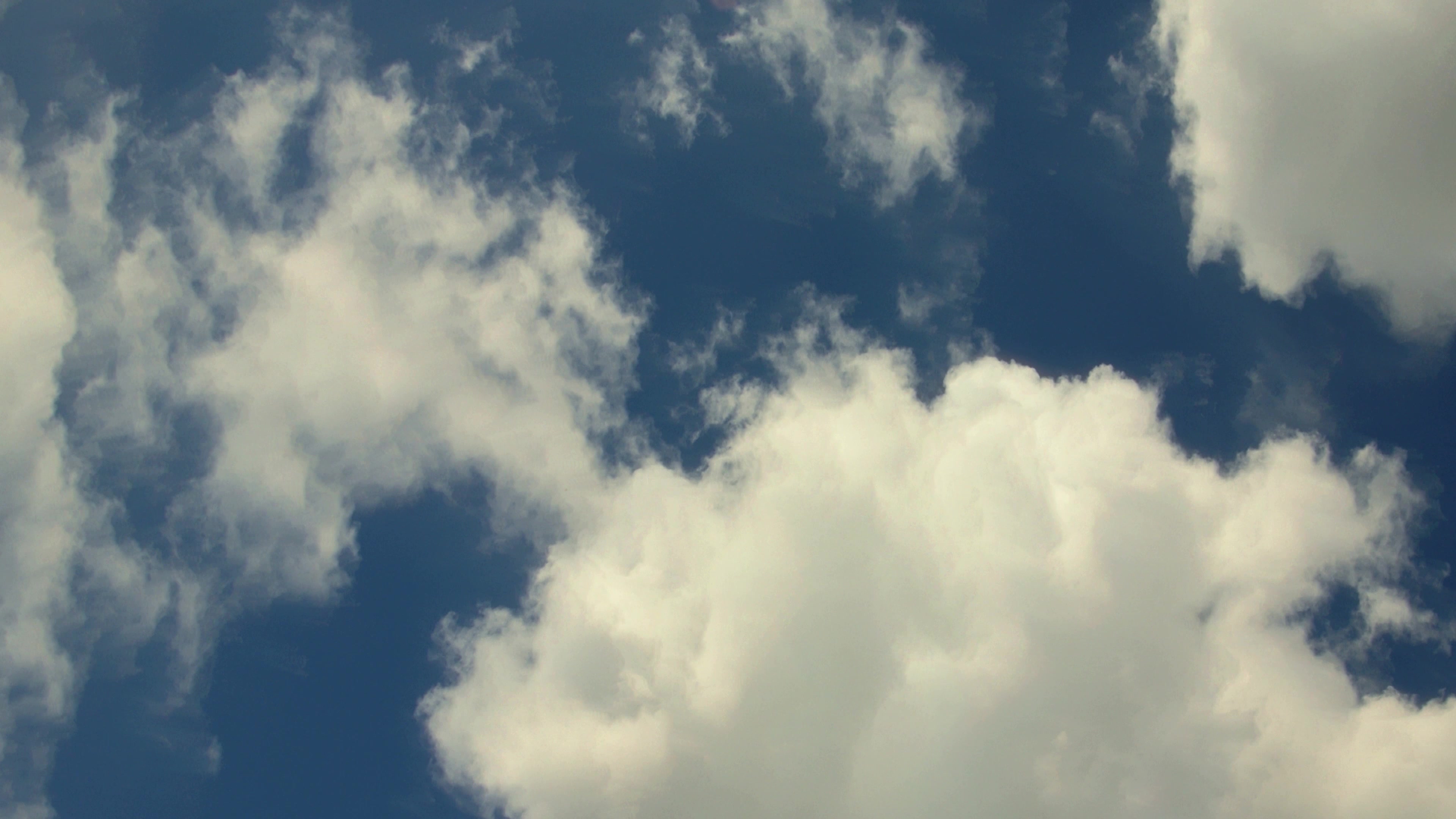 4K video of fluffy white time-lapse clouds drifting over deep blue sky.