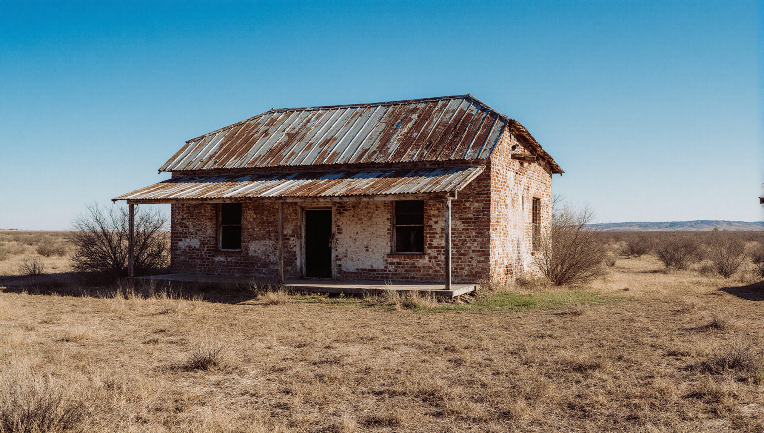 Weathered brick house in vast, dry landscape with blue sky.