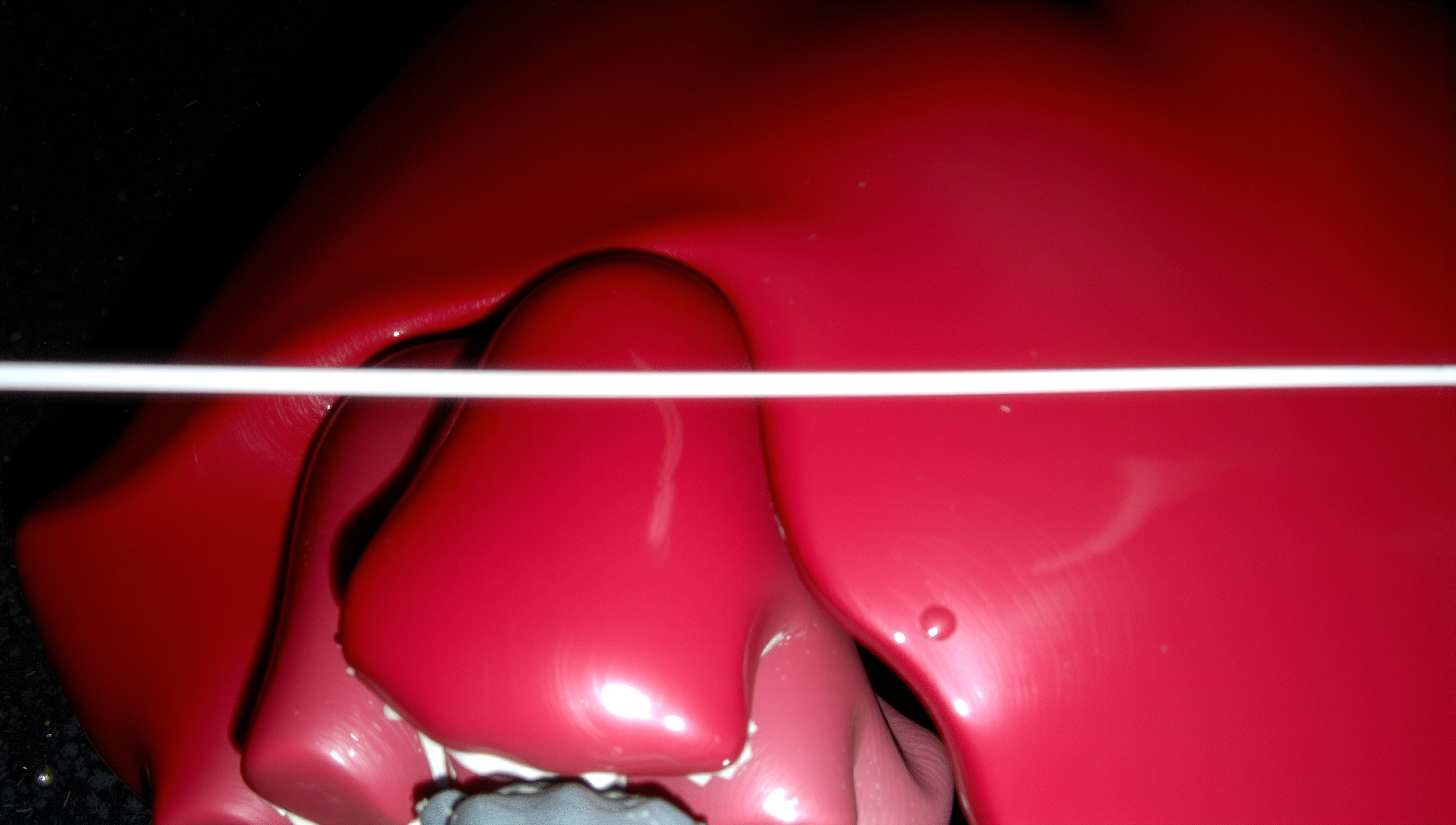 Close-up of a glossy red heart sculpture with a white rod crossing above on a dark background.
