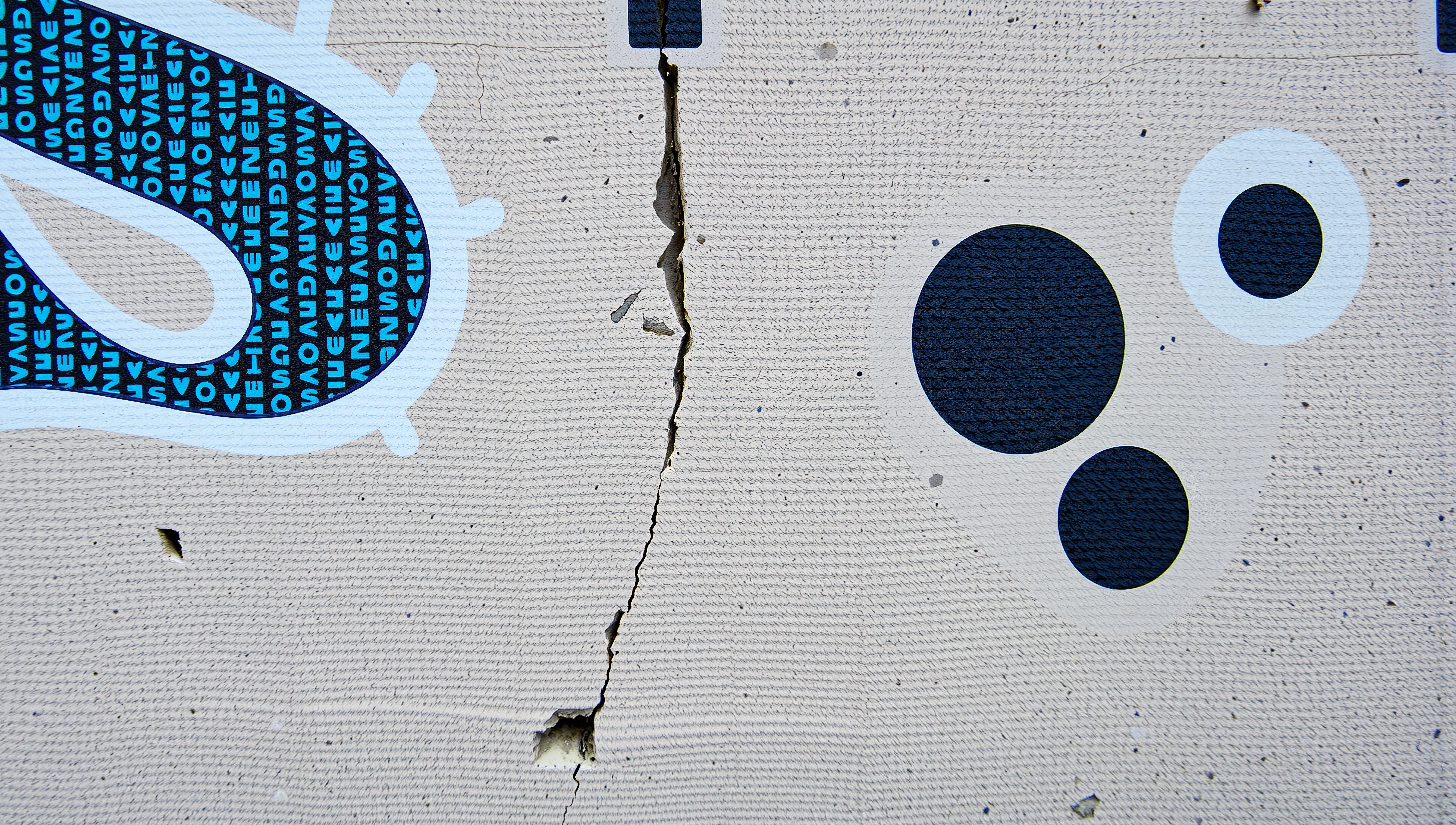 Abstract mural art on textured concrete wall showing geometric patterns with a central crack.